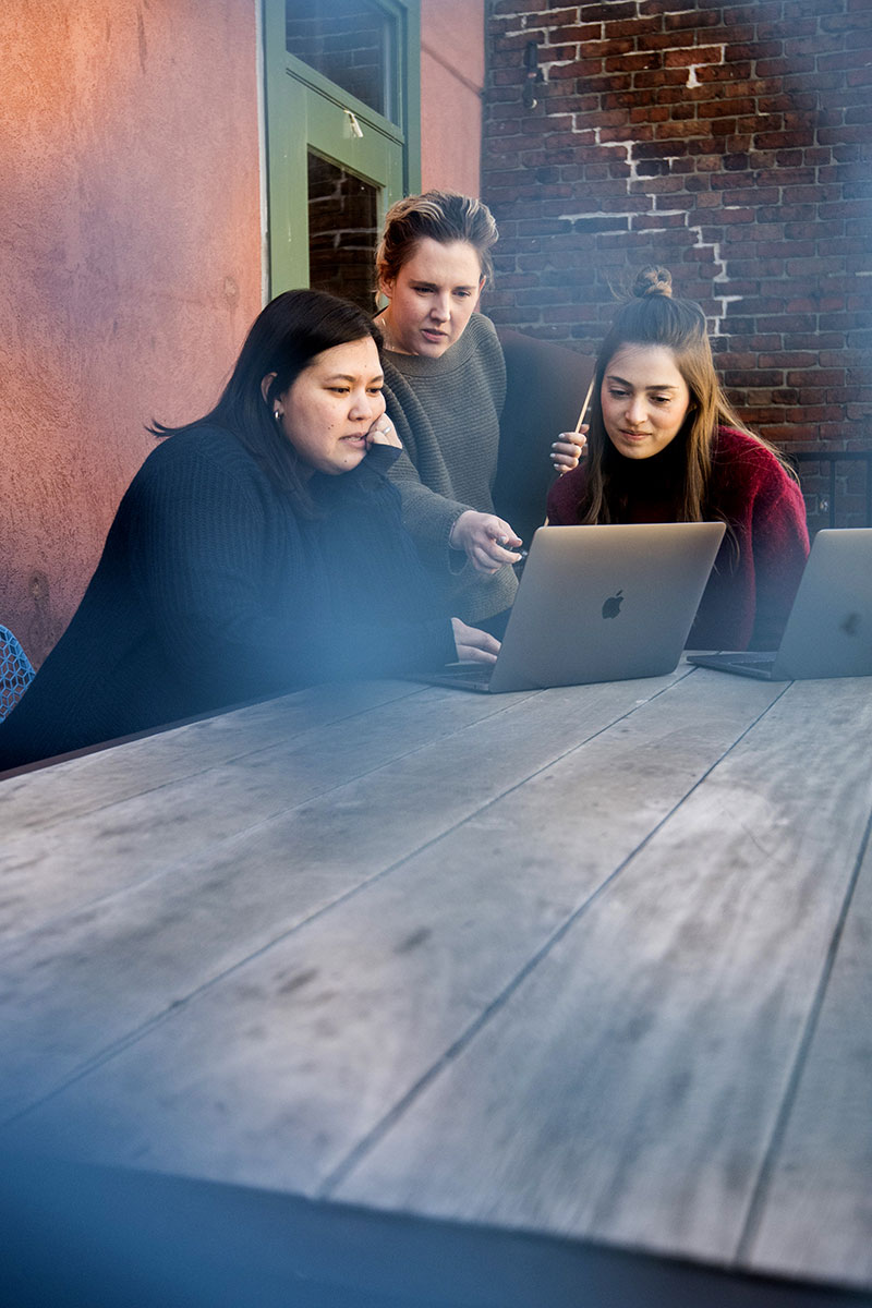 Tatiana, Caitlyn and Jess huddle around a computer on our roof deck
